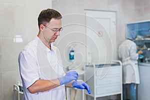 Closeup of a caucasian doctor man, wearing a white coat, putting on a pair of blue surgical gloves