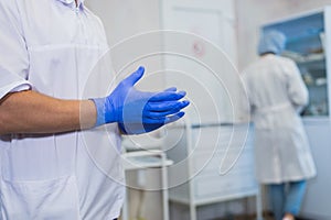 Closeup of a caucasian doctor man, wearing a white coat, putting on a pair of blue surgical gloves