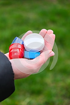 Closeup at caucasian female hands full of colorful plastic bottle cups, handful of waste of plastic lids. Recycling. Collecting