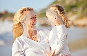Closeup of a caucasian girl laughing while enjoying a day out with her mother at the beach. Mom and daughter enjoying a