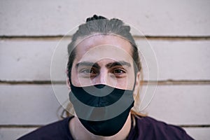 closeup caucasian young man with long hair black t-shirt and face mask looking at camera