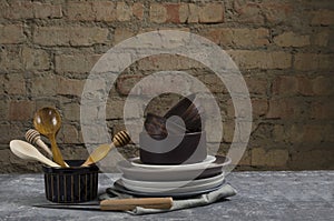 Closeup of cay, ceramic plates and bowls, wooden spoons, napkin on the rustic kitchen table against old brick wall.Empty space for