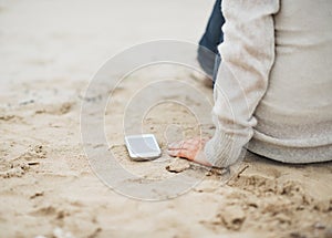 Closeup on cell phone near woman sitting on beach