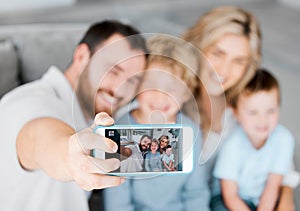Closeup of cellphone screen showing happy caucasian family taking selfies at home. Loving parents capturing photos and