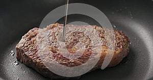 Closeup of checking temperature of ribeye steak in a non stick pan