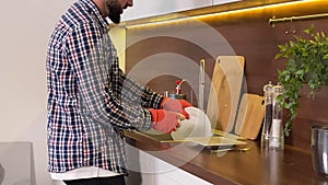 Closeup of cheerful adult man washing dishes at kitchen sink at home