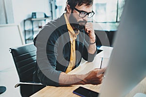 Closeup of cheerful bearded designer in eye glasses working at sunny loft studio.Man using contemporary desktop computer