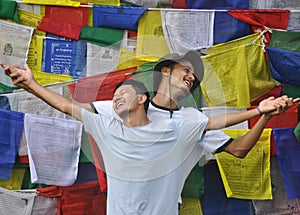Closeup of cheerful two male friends looking sideways, spreading hands against buddhist prayer flags