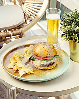 Closeup of a cheese burger with potato chips and a a glass of beer on a balcony table