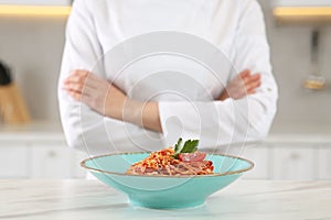 Closeup of chef with crossed arms near delicious spaghetti in kitchen, focus on food