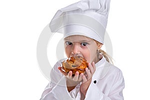 Closeup of a chef girl in a cap cook uniform, holding and biting the tasty bun. Looking at the camera