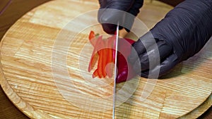 Closeup of chef hands in gloves slicing red sweet pepper on wooden cutting board