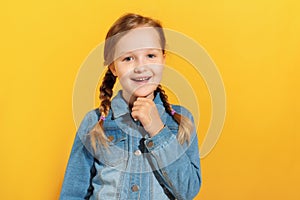 Closeup of a child in a denim shirt on a yellow background. Little girl smiles and looks at the camera