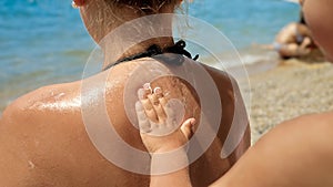 Closeup of child helping his mother applying sunscreen UV protection lotion on sea beach during summer holiday vacation