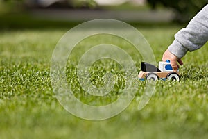 Closeup of child`s hand playing with toy cay on the green grass in the park. Toddler boy playing with small car