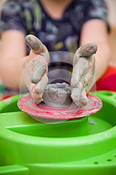 Closeup of child`s hands with potter`s wheel. Kid boy making a bowl of clay at pottery school