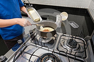 Closeup of child`s hands spooning a piece of butter into the pan with condensed milk and cocoa powder