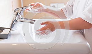 Closeup of a child`s soapy hands being washed under running water in a sink