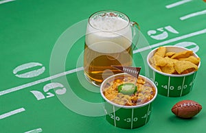 Closeup of chili and mug of beer and football decorations on tab