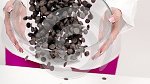 Closeup chocolatier pours dark chocolate chips on white background, slow motion
