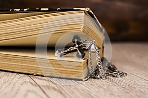 Closeup of Christian cross with silver chain on blank open book with a black wooden background