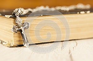 Closeup of Christian cross with silver chain on blank open book with a black wooden background