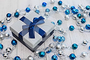 Closeup Christmas gift with blue ribbon and silver and blue Christmas balls on white wooden background