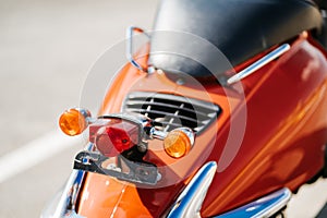 Closeup chrome detail and taillight and turn signals of orange retro vintage scooter.