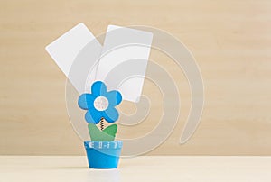 Closeup clamp photo in blue flower shape shape in flowerpot with black white paper on blurred wooden desk and wall background