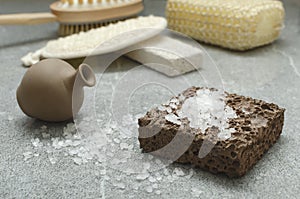 Closeup of clay bottle of aroma oil, stone and sea salt for scrubing, sponges on the grey surface