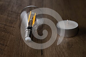 Closeup of a clear light bulb next to a small candle on a wooden surface