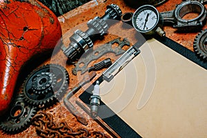 Closeup clipboard with vintage paper in the center of tools, gears on metal background. Motorcycle tools, equipment and repair