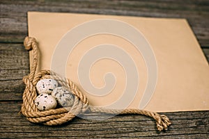 Closeup coil of rope with quail eggs on sheet of paper for text on rustic wood board