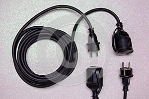 Closeup of a coiled black electric power extension cable with a further plug and socked on a bright glittering background. Space
