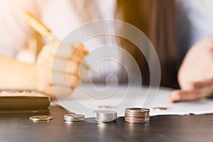 Closeup coins on the desk with businesswoman working on desk office holding pen and using a calculator to calculate the numbers.