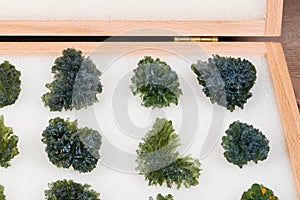 Closeup a collection of raw green moldavite gems in wooden storage locker