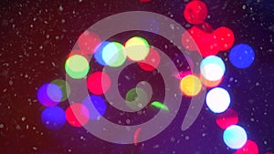 Closeup colorful blinking Christmas garland lights bokeh background surrounded by falling snowflakes