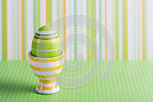 Closeup colorful painted Easter egg in vibrant modern egg stand on striped green background
