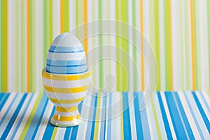 Closeup colorful painted Easter egg in vibrant modern egg stand on striped green and blue background