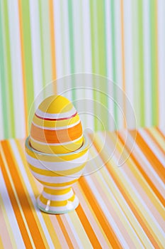 Closeup colorful painted Easter egg in vibrant modern egg stand on striped green and orange background