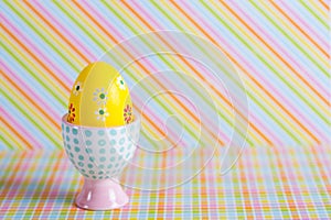 Closeup colorful painted Easter egg in vibrant modern egg stand on striped rainbow background
