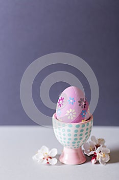 Closeup colorful painted Easter egg in vibrant modern egg stand surrounded by white flowering tree branches on gray background