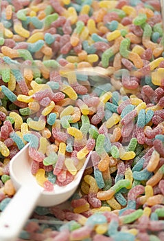 Closeup of colorful sour worms candy sweets in transparent box with white scoop.