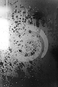 Closeup of condensation patterns on glass window, water droplets with light reflection and refraction, black and white