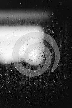 Closeup of condensation patterns on glass window, water droplets with light reflection and refraction, black and white