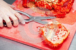 Closeup cook hand cuts pork fillet steak with sharp knife on red plastic cutting board on metal table in restaurant kitchen.