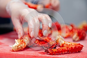 Closeup cook hand cuts pork fillet steak with sharp knife on red plastic cutting board on metal table in restaurant kitchen.