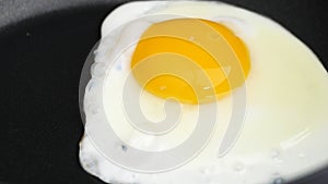 Closeup of cooking fried eggs in black frying pan. Breakfast concept.