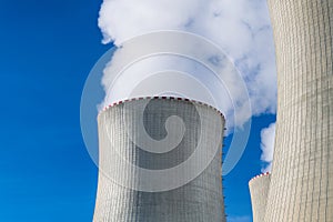 Closeup of cooling towers power station with white clouds of steam on blue sky background