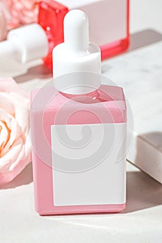 Closeup of cosmetic bottle with a dropper with oil based on rose extract oil on a marble background with flowers. Mockup